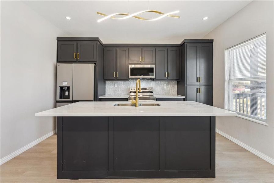 Kitchen with a center island with sink, backsplash, appliances with stainless steel finishes, light wood-style floors, and a sink