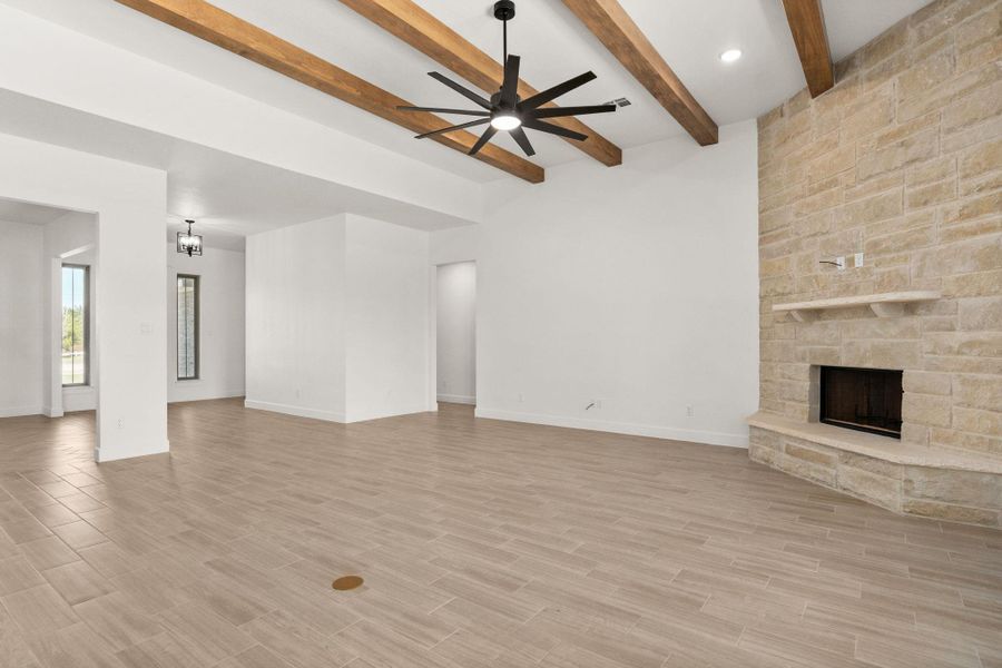 Unfurnished living room with a stone fireplace, wood tiled floors, a ceiling fan, beamed ceiling, and a chandelier