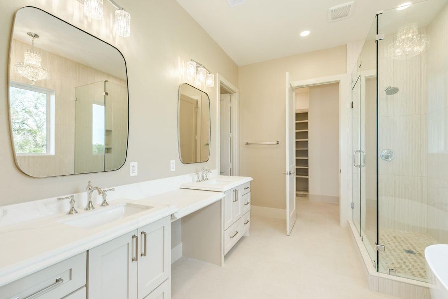 This spacious and elegant bathroom features dual sinks with modern fixtures, large mirrors, and chic pendant lighting. It includes a walk-in shower with glass doors and a neutral color palette for a serene atmosphere.