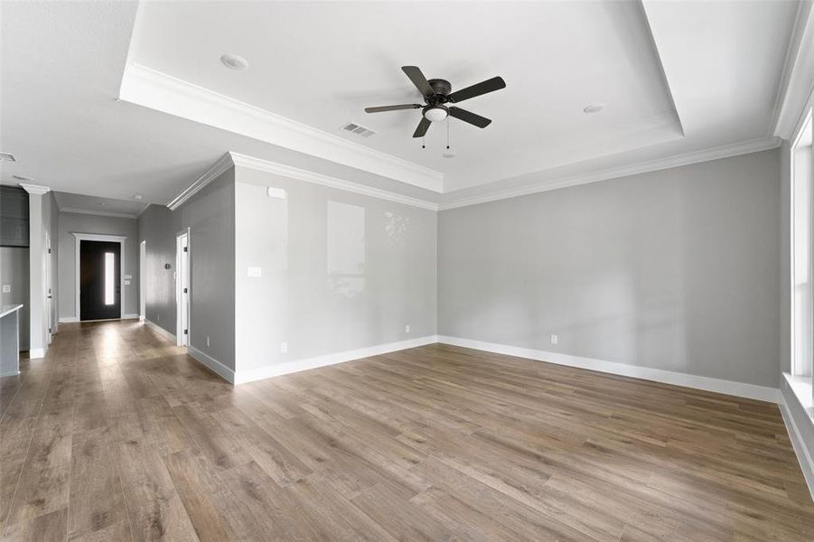 Empty room featuring a raised ceiling, ornamental molding, wood finished floors, and a ceiling fan