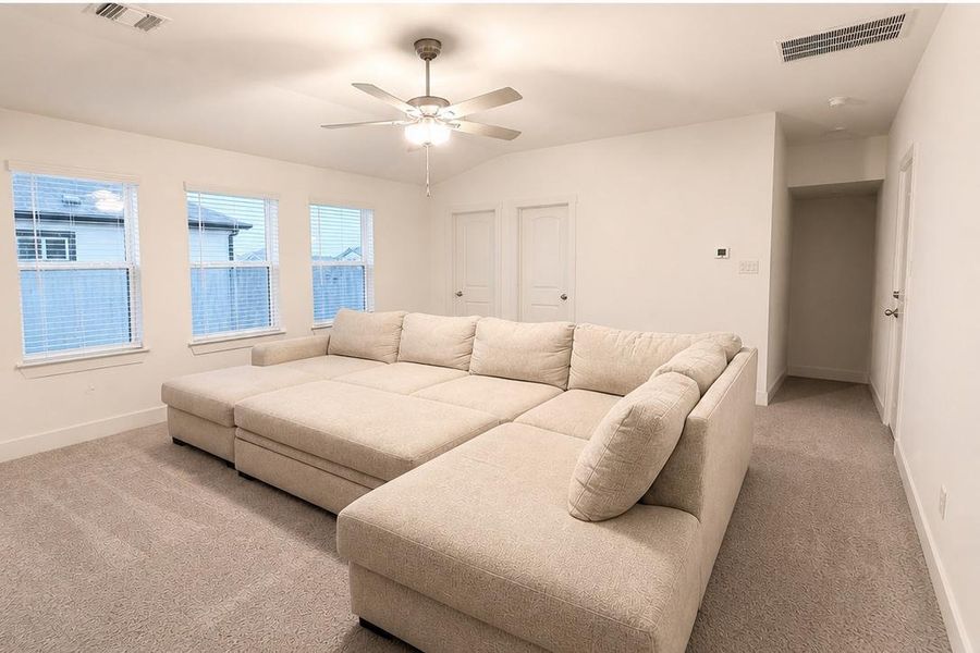 Bright living area featuring neutral carpeting, multiple windows with blinds, a ceiling fan with integrated lighting, and white walls Bright living area featuring neutral carpeting, multiple windows with blinds, a ceiling fan with integrated lighting, and white walls
