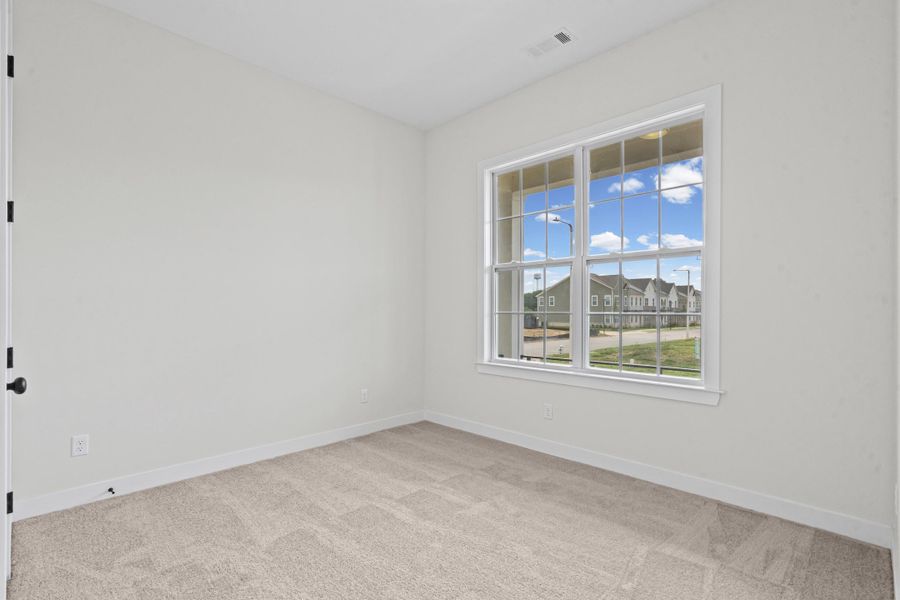 Bright room featuring a large multi-pane window, neutral wall paint, white trim, and a textured carpet Bright room featuring a large multi-pane window, neutral wall paint, white trim, and a textured carpet
