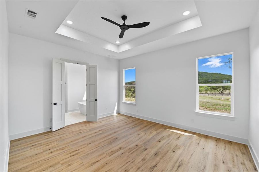 Unfurnished bedroom featuring light wood-style floors, a raised ceiling, a ceiling fan, recessed lighting, and ensuite bathroom Unfurnished bedroom featuring light wood-style floors, a raised ceiling, a ceiling fan, recessed lighting, and ensuite bathroom