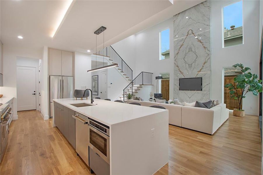 Kitchen with a kitchen island with sink, sink, light hardwood / wood-style flooring, gray cabinets, and hanging light fixtures