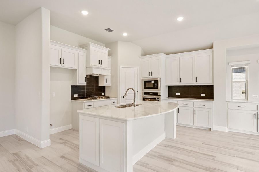 Kitchen with white cabinets, center island with sink, stainless steel appliances, and dark tile backsplash Kitchen with white cabinets, center island with sink, stainless steel appliances, and dark tile backsplash