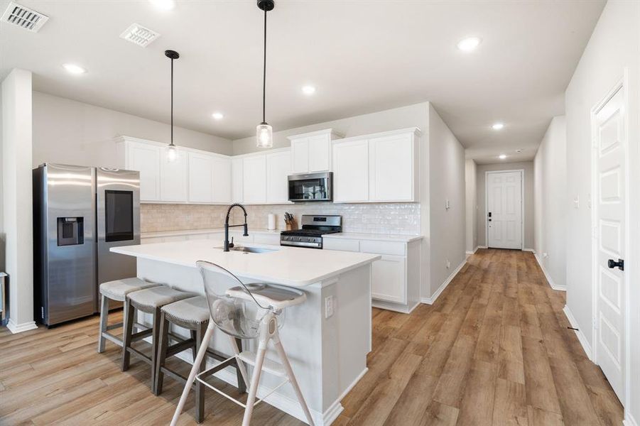 Kitchen featuring stainless steel appliances, white cabinetry, a breakfast bar area, decorative backsplash, and an island with sink Kitchen featuring stainless steel appliances, white cabinetry, a breakfast bar area, decorative backsplash, and an island with sink
