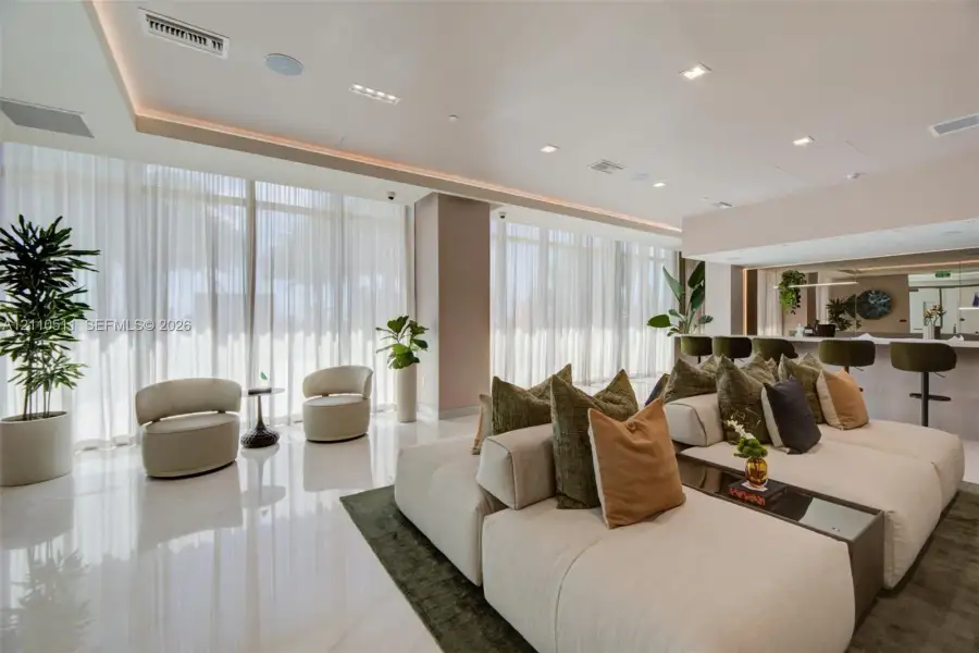 Open-concept interior featuring polished stone flooring, expansive floor-to-ceiling windows with integrated drapery tracks, recessed cove lighting, and a built-in refreshment bar