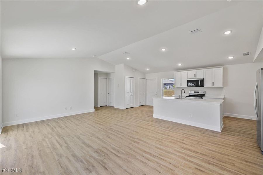 Kitchen with white cabinets, open floor plan, an island with sink, light countertops, and vaulted ceiling