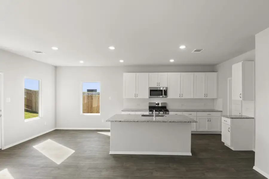 Image of a kitchen with a white center island and cabinets with granite countertops and black appliances with a dining area to the left