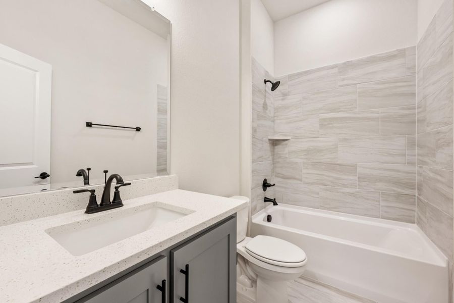 Full bathroom with gray vanity, quartz countertop, and tiled tub-shower combo with dark fixtures Full bathroom with gray vanity, quartz countertop, and tiled tub-shower combo with dark fixtures