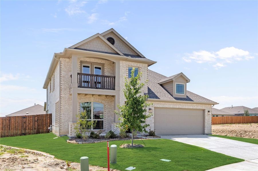 Two-story brick home with second-floor balcony, two-car garage, and green front lawn