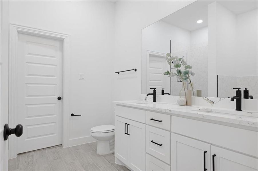 Bathroom featuring double vanity, a sink, toilet, and baseboards