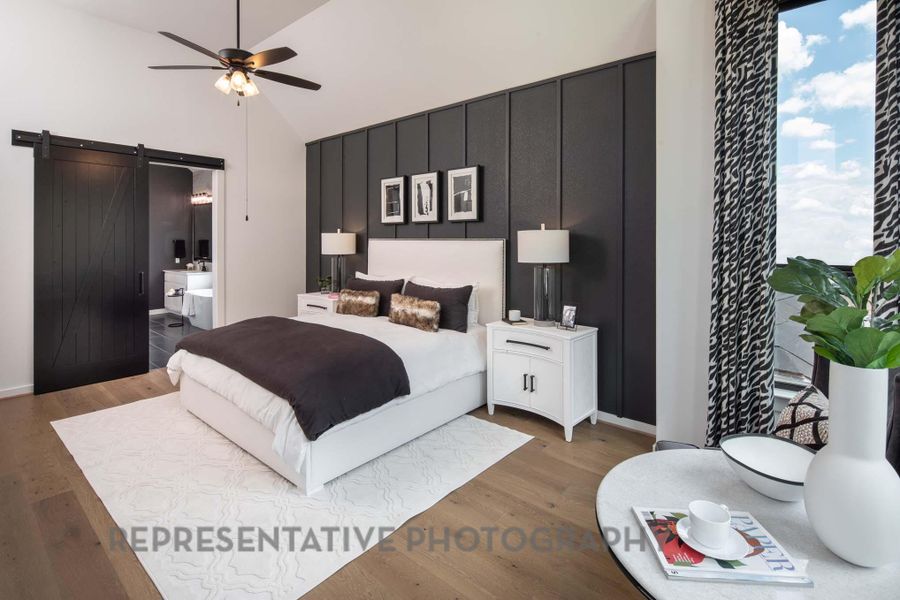 Bedroom with a barn door, wood finished floors, connected bathroom, high vaulted ceiling, and ceiling fan Bedroom with a barn door, wood finished floors, connected bathroom, high vaulted ceiling, and ceiling fan