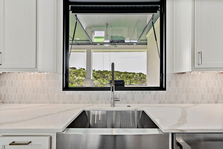 A sleek stainless steel farmhouse sink is complemented by bright white cabinetry and a geometric tile backsplash.