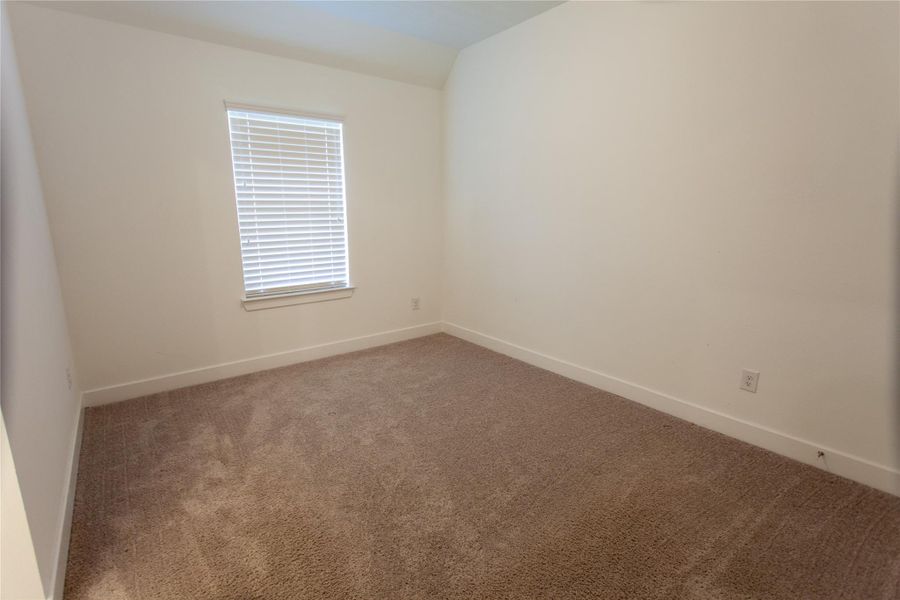 A peaceful secondary bedroom with a vaulted ceiling, plush carpet, and a sun-filled window — a flexible space ideal as a guest room, nursery, or home office.