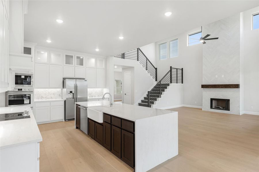 Open-concept kitchen with large island, white cabinets, stainless appliances, and fireplace in adjoining living area
