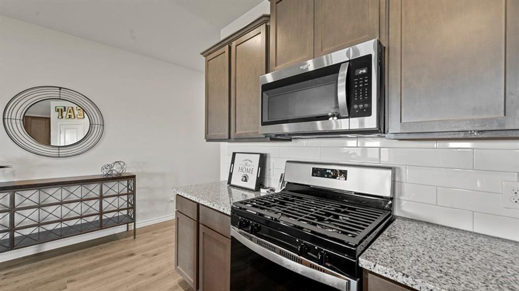 Kitchen with stainless steel appliances, light stone counters, tasteful backsplash, light wood finished floors, and dark brown cabinets