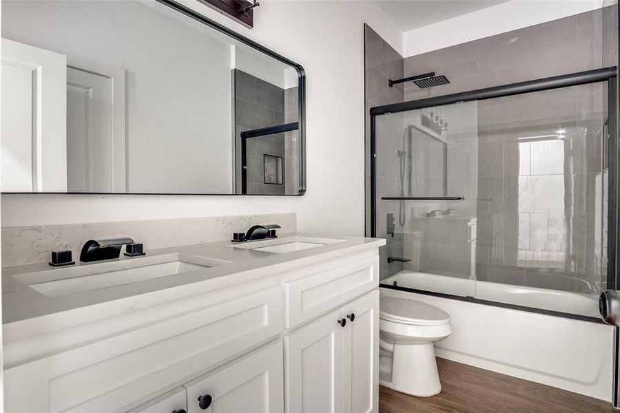 Bathroom featuring combined bath / shower with glass door, double vanity, and dark wood-type flooring