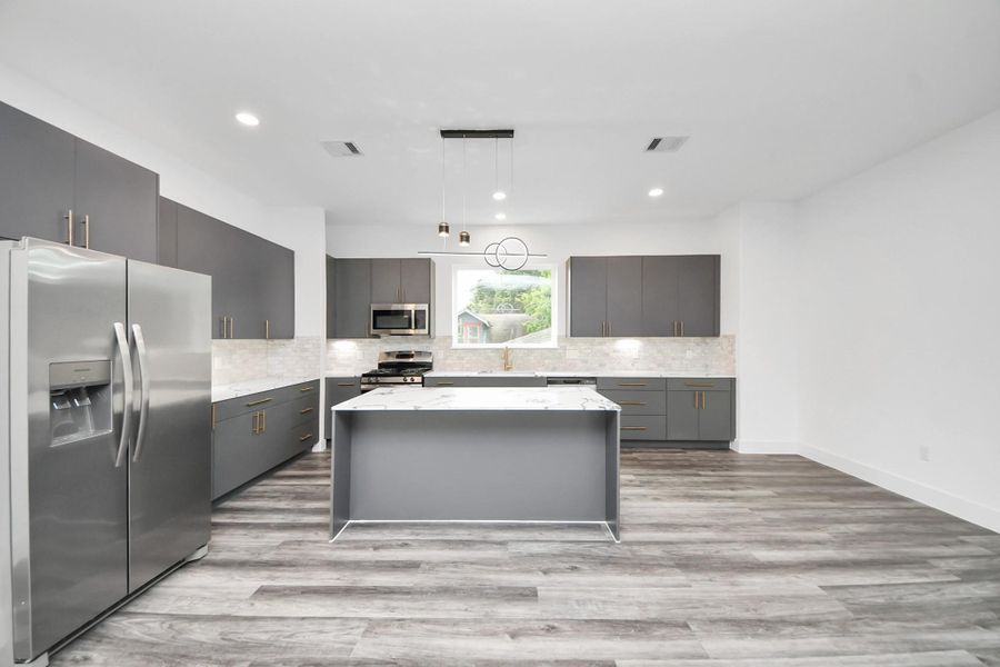 This modern kitchen features sleek gray cabinetry, stainless steel appliances, and a central island with a marble-look countertop. The open layout is complemented by wood-style flooring and a large window providing natural light. This modern kitchen features sleek gray cabinetry, stainless steel appliances, and a central island with a marble-look countertop. The open layout is complemented by wood-style flooring and a large window providing natural light.