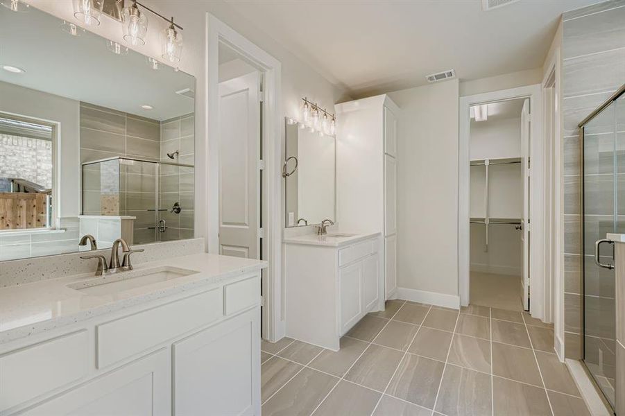 Full bath featuring a stall shower, two vanities, light tile patterned flooring, and a walk in closet