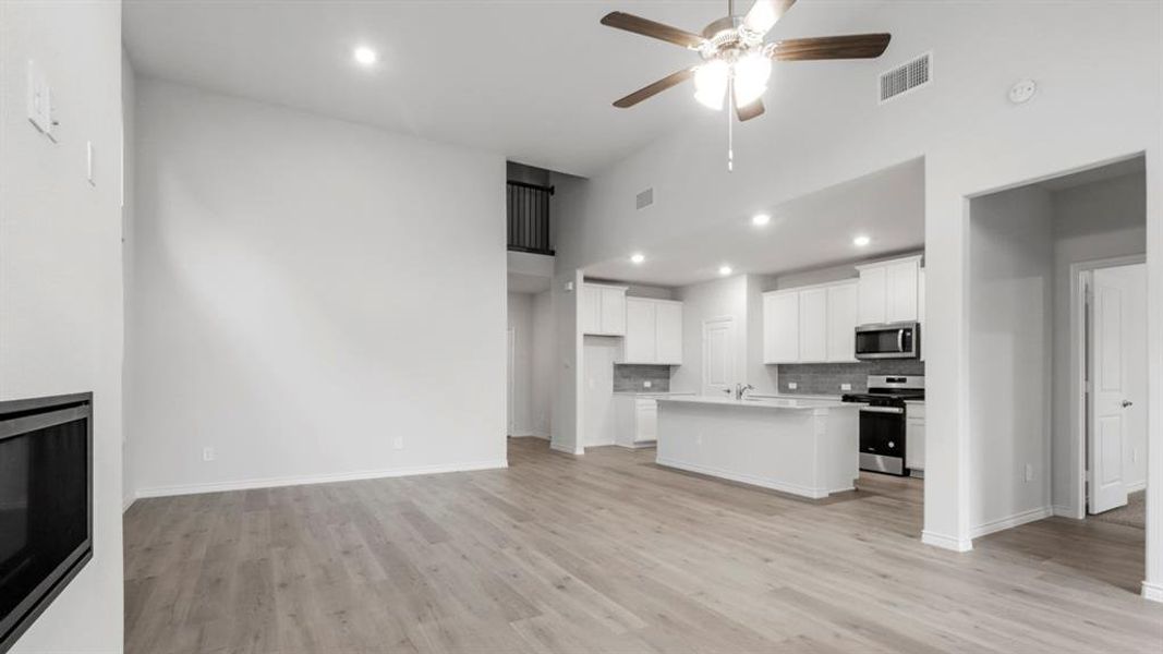 Unfurnished living room with recessed lighting, ceiling fan, light wood finished floors, and a high ceiling