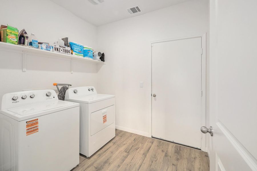 Dedicated laundry area featuring wood-finish flooring, a wall-mounted storage shelf, and a ceiling-mounted light fixture Dedicated laundry area featuring wood-finish flooring, a wall-mounted storage shelf, and a ceiling-mounted light fixture