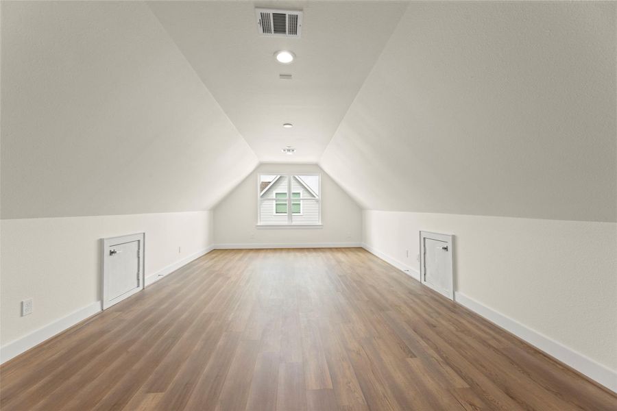 This photo showcases a spacious, well-lit 2nd living or office space with sloped ceilings, there is a window at the far end providing natural light, and doors on the side walls for additional storage. Ideal for a cozy retreat or storage area.