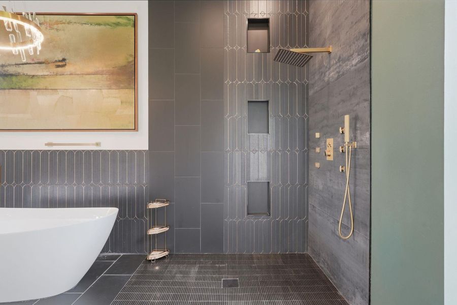 This bathroom features a modern design with sleek dark tiles, a luxurious rainfall showerhead, and built-in shelving. It also includes a stylish freestanding bathtub and contemporary artwork, creating a sophisticated and relaxing atmosphere.