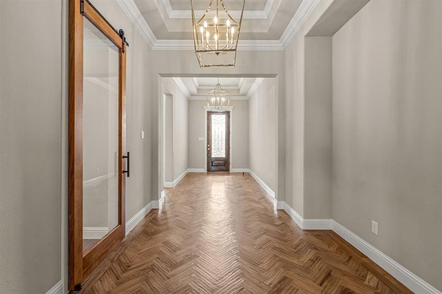 Foyer entrance featuring a tray ceiling, a barn door, a chandelier, and ornamental molding