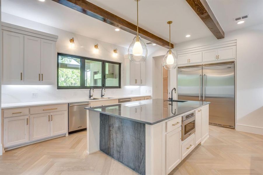 Kitchen featuring built in appliances, parquet floors, a center island with sink, hanging light fixtures, and beam ceiling