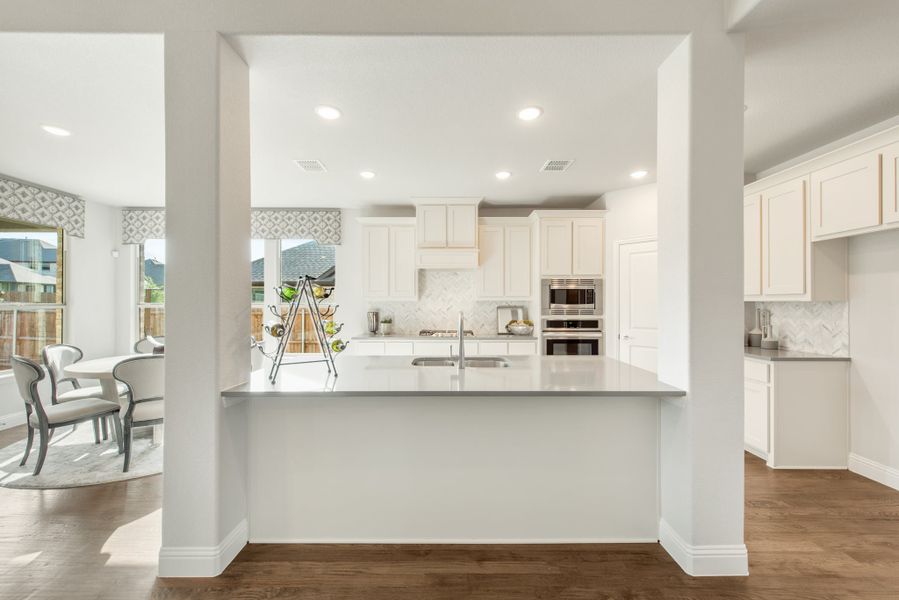 Open kitchen with white cabinets, gray island, stainless steel appliances, and hardwood floors open to dining area