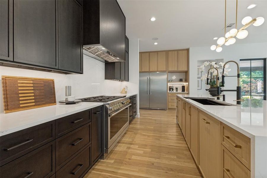 Contemporary kitchen featuring light wood-finish flooring, a spacious center island with a black sink and matte black faucet, and white countertops Contemporary kitchen featuring light wood-finish flooring, a spacious center island with a black sink and matte black faucet, and white countertops