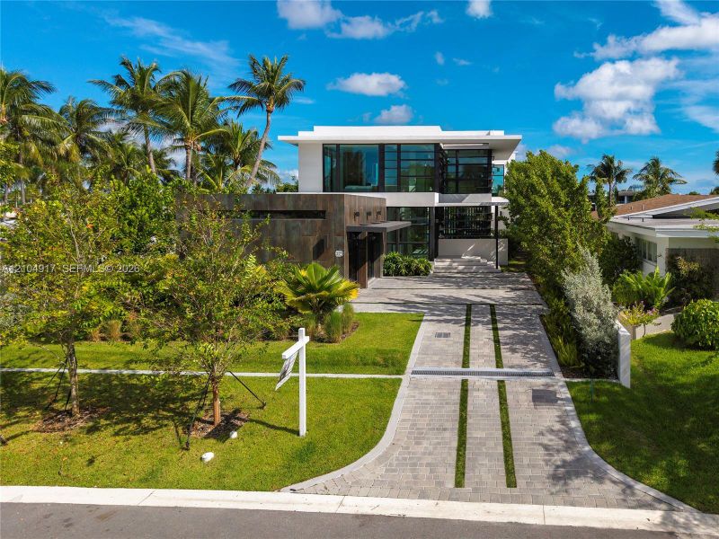 Contemporary two-story exterior featuring floor-to-ceiling windows, a metallic-finish facade, integrated hardscaping, and a paver driveway with turf accents