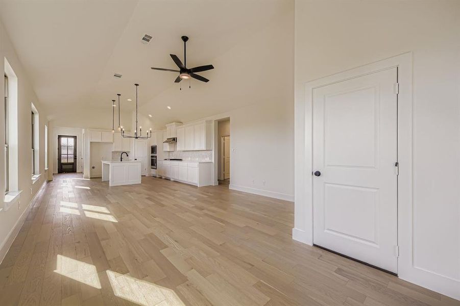 Unfurnished living room featuring light wood-style flooring, a ceiling fan, a chandelier, and high vaulted ceiling Unfurnished living room featuring light wood-style flooring, a ceiling fan, a chandelier, and high vaulted ceiling