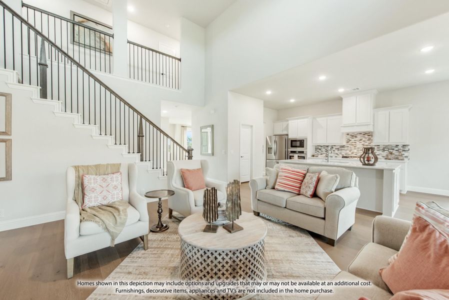 Open-concept living room with two-story ceiling, staircase, and kitchen visible in background Open-concept living room with two-story ceiling, staircase, and kitchen visible in background
