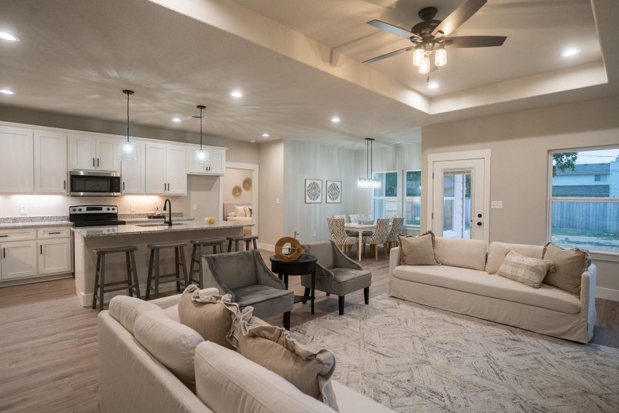 Living room with recessed lighting, light wood finished floors, a ceiling fan, and a tray ceiling