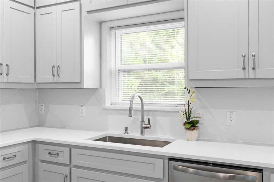 Kitchen featuring plenty of natural light, stainless steel dishwasher, and light stone countertops Kitchen featuring plenty of natural light, stainless steel dishwasher, and light stone countertops