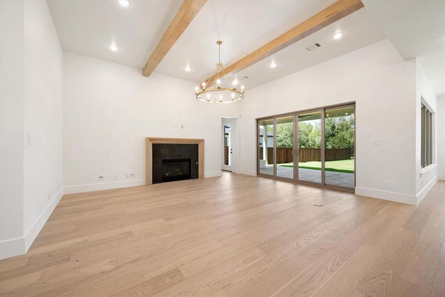 Unfurnished living room with light wood-type flooring, beam ceiling, and a notable chandelier