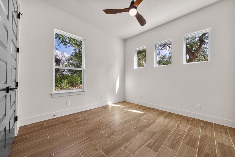 A well-lit room featuring rich wood-look tile flooring and views of mature trees from multiple windows.