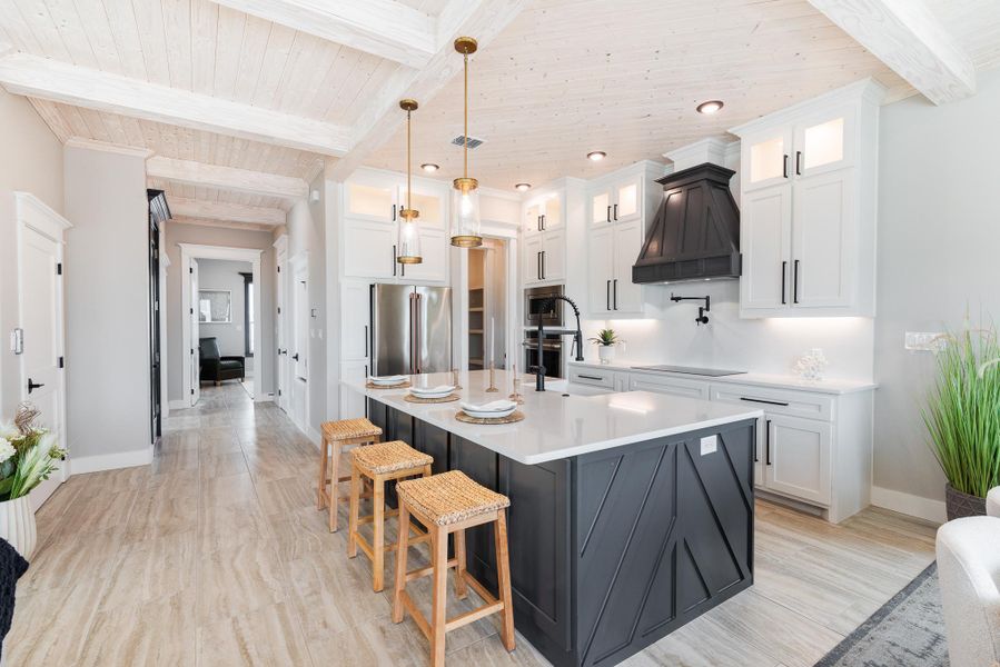 Kitchen featuring stainless steel appliances, a wood ceiling with exposed beams, custom range hood, light countertops, and light wood-style floors Kitchen featuring stainless steel appliances, a wood ceiling with exposed beams, custom range hood, light countertops, and light wood-style floors