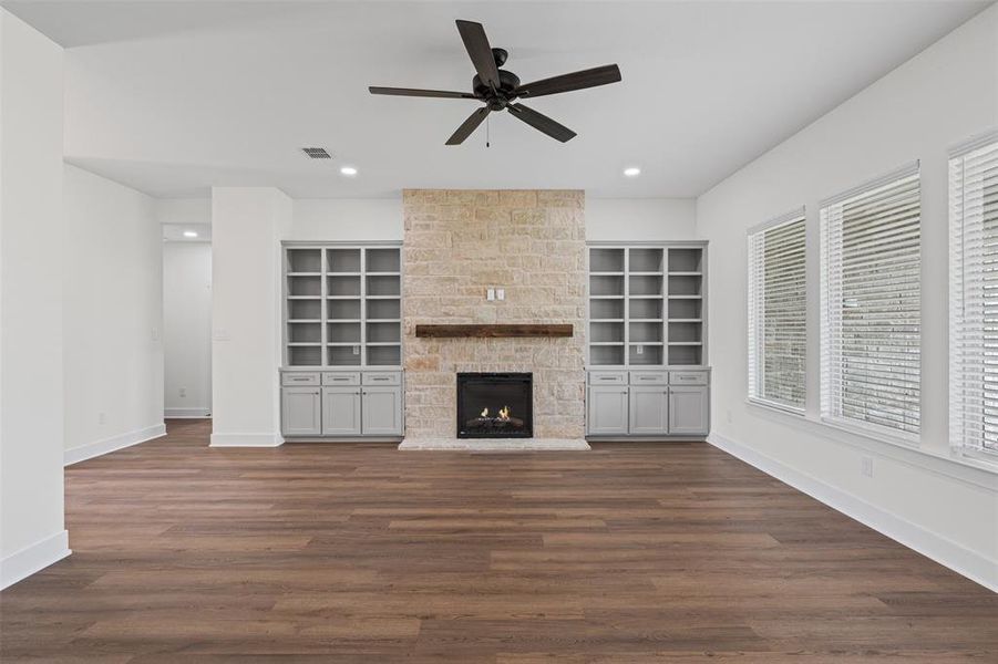 Living space featuring wood-look flooring, a stone-clad fireplace with a wood mantle, and built-in shelving with cabinetry