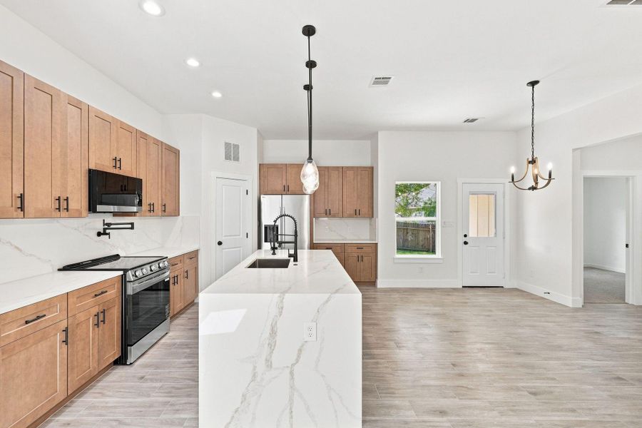 Expansive waterfall quartz kitchen island with an undermount sink and a sleek matte black gooseneck faucet.