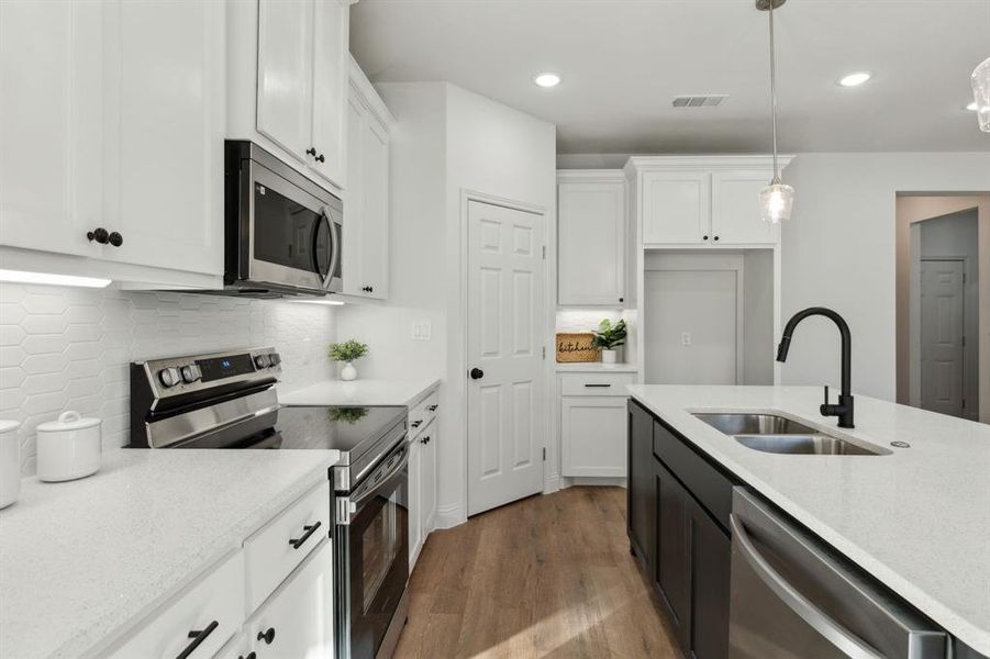 Kitchen with appliances with stainless steel finishes, tasteful backsplash, sink, white cabinets, and hanging light fixtures