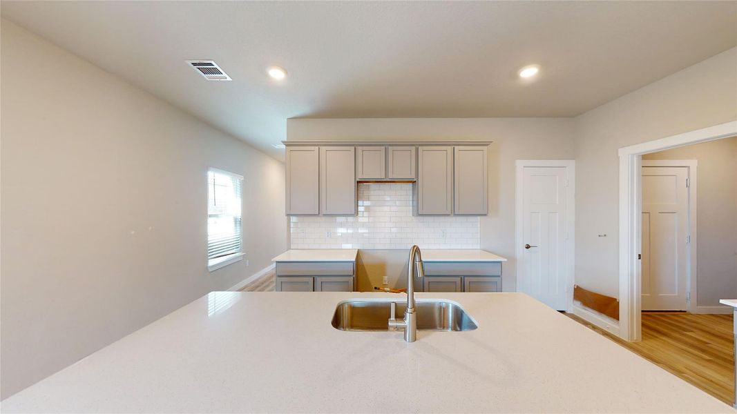 Kitchen with gray cabinets, backsplash, light wood-style floors, recessed lighting, and light stone counters