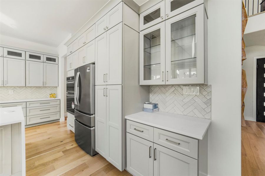 Bright, modern kitchen featuring ample white cabinetry, sleek stainless steel appliances, and a stylish herringbone backsplash. The space is enhanced by natural light and warm wood flooring, creating a welcoming atmosphere.