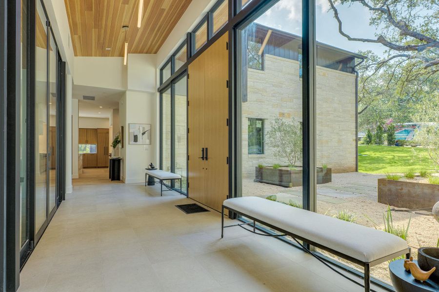 A spacious entrance hall with tall ceilings features a wall of glass overlooking a meticulously landscaped yard. A spacious entrance hall with tall ceilings features a wall of glass overlooking a meticulously landscaped yard.