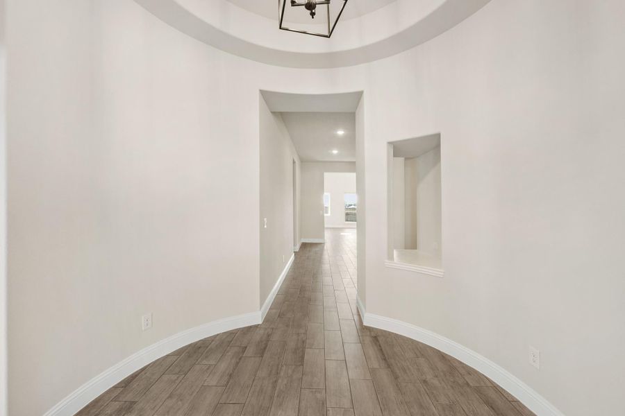 Round foyer with coffered ceiling, pendant light, wood-look tile floors, and wall niche leading to hallway Round foyer with coffered ceiling, pendant light, wood-look tile floors, and wall niche leading to hallway