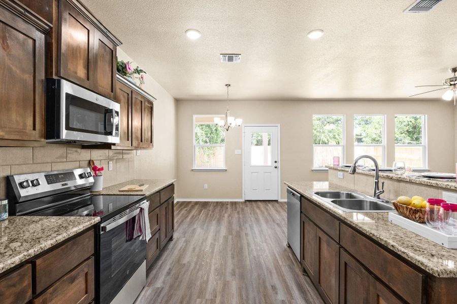 Kitchen with dark brown cabinetry, stainless steel appliances, tasteful backsplash, light stone counters, and a textured ceiling