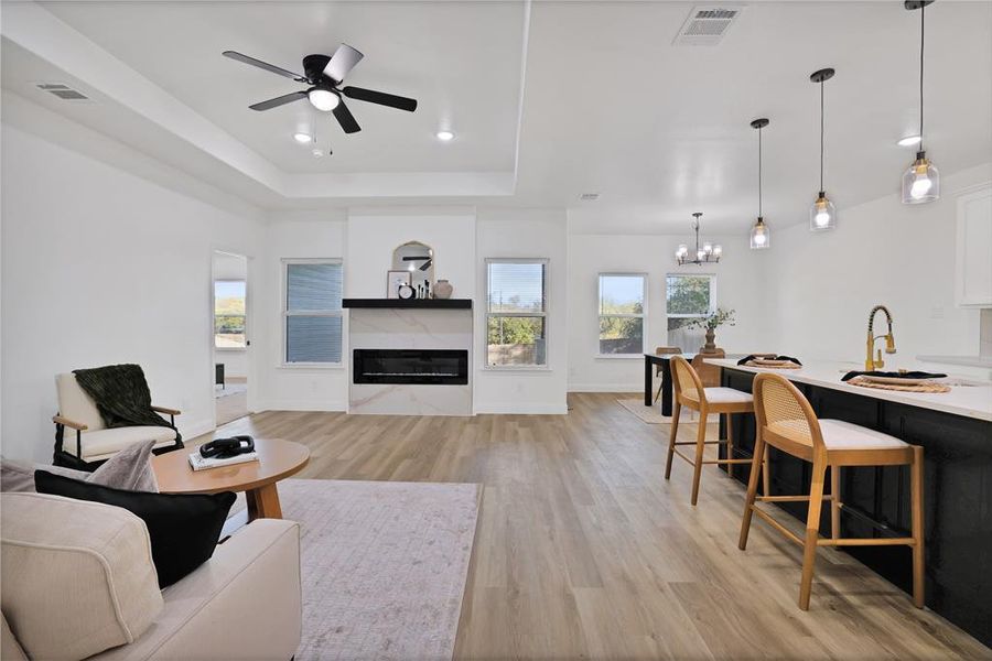 Living room featuring ceiling fan with notable chandelier, a raised ceiling, and light wood-type flooring