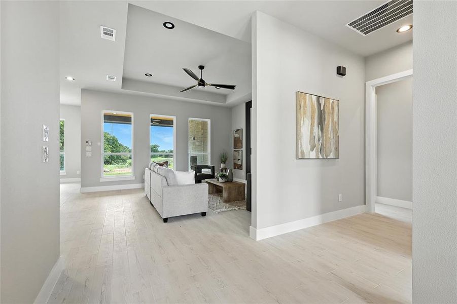 Living area with light wood-style flooring, a ceiling fan, recessed lighting, and a tray ceiling